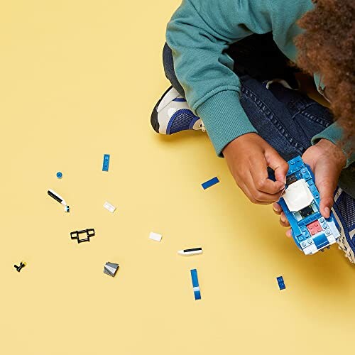 Child assembling a blue and white LEGO car on a yellow surface.